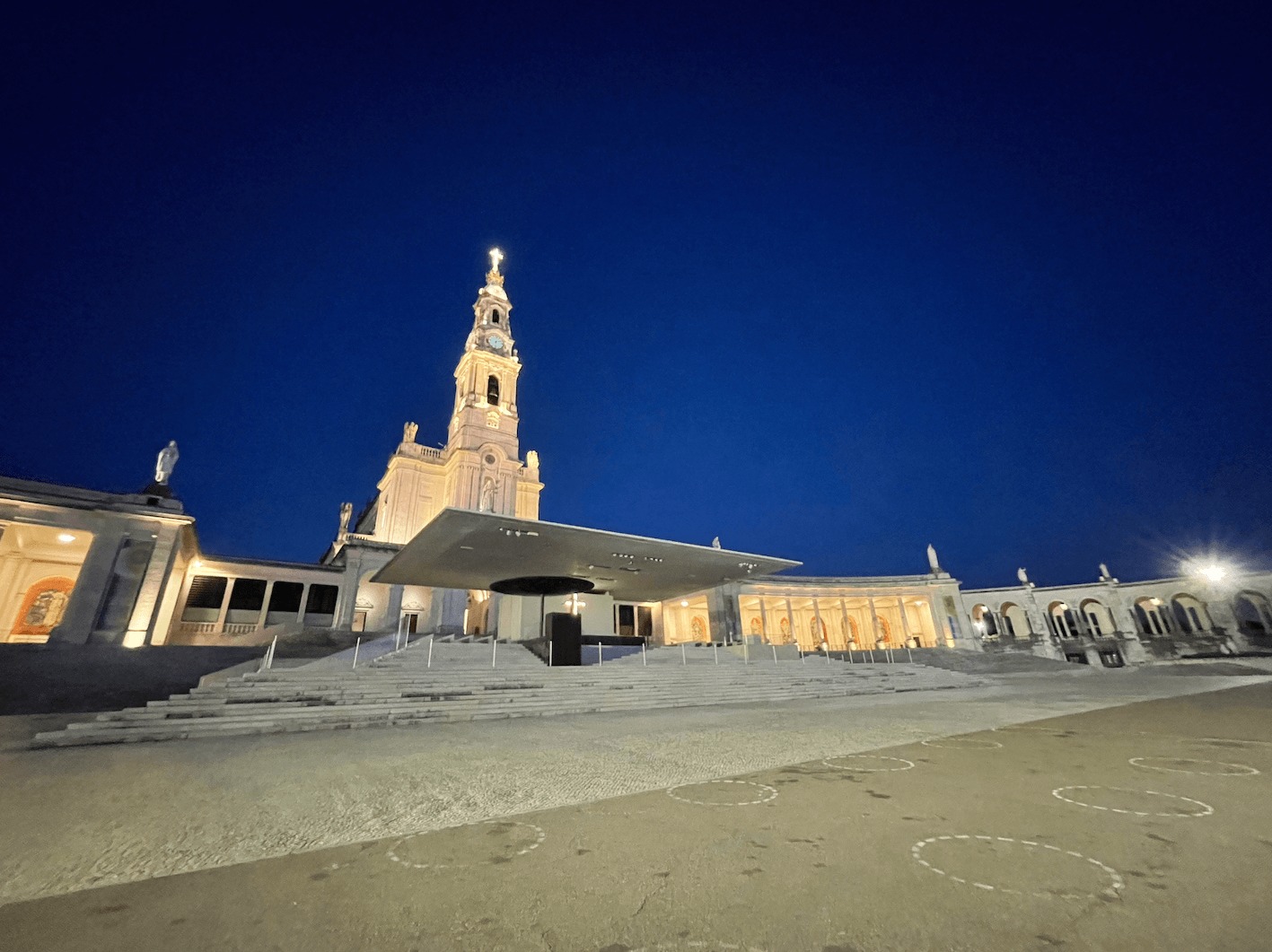 Foto noturna da frente do Santuário de Fátima que está iluminado, não há pessoas na foto.