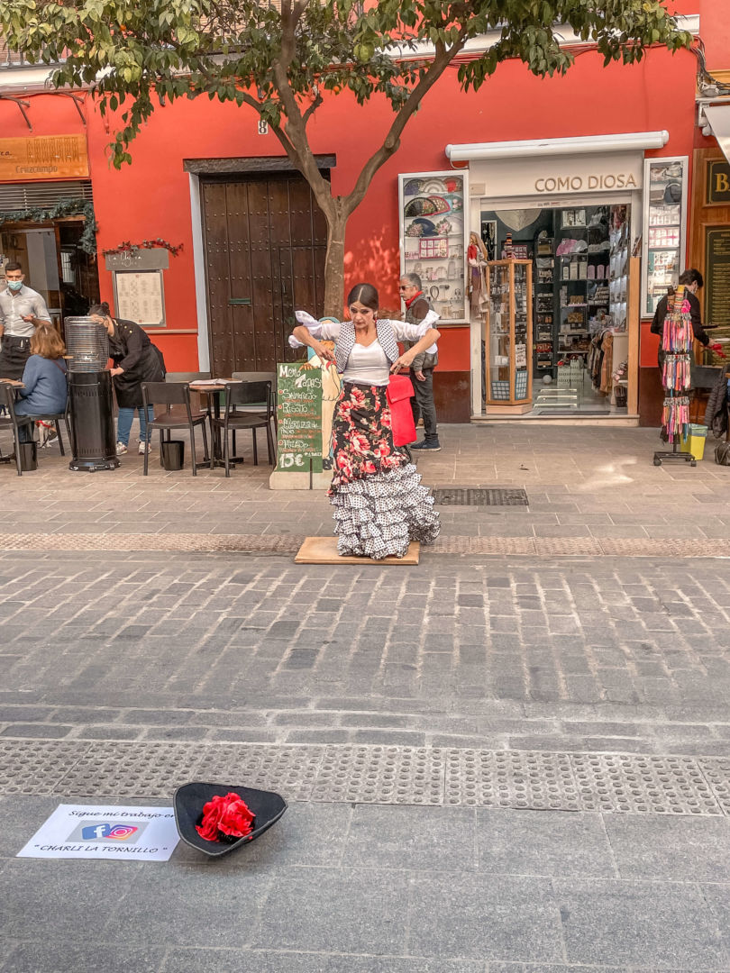 Uma dançarina de rua de flamenco, com uma saia florida rodada e castanholas na mão em meio a dança. 