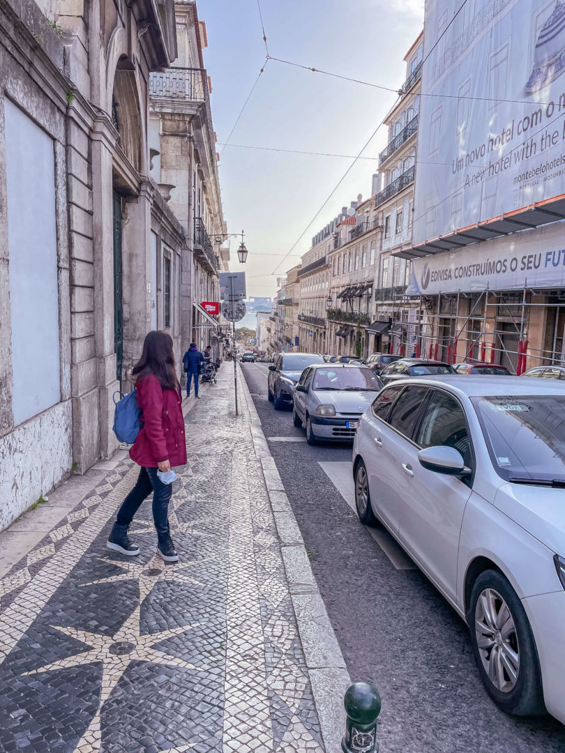 Foto de uma das ruas de Lisboa. Eu estou em segundo plano, olhando para trás. Não é possível ver meu rosto.