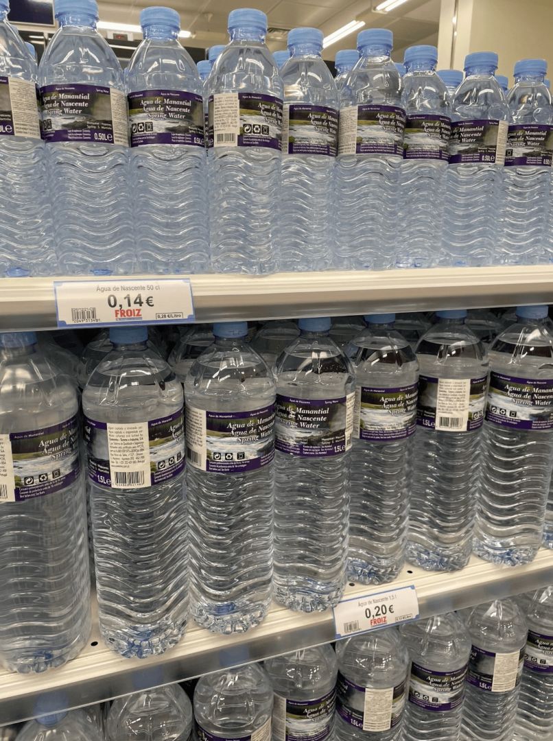 Águas em garrafa de plástico nas prateleiras de um supermercado, É possível ver a etiqueta do preço, 0,14 euros a pequena e 0,20 euros a de um litro.