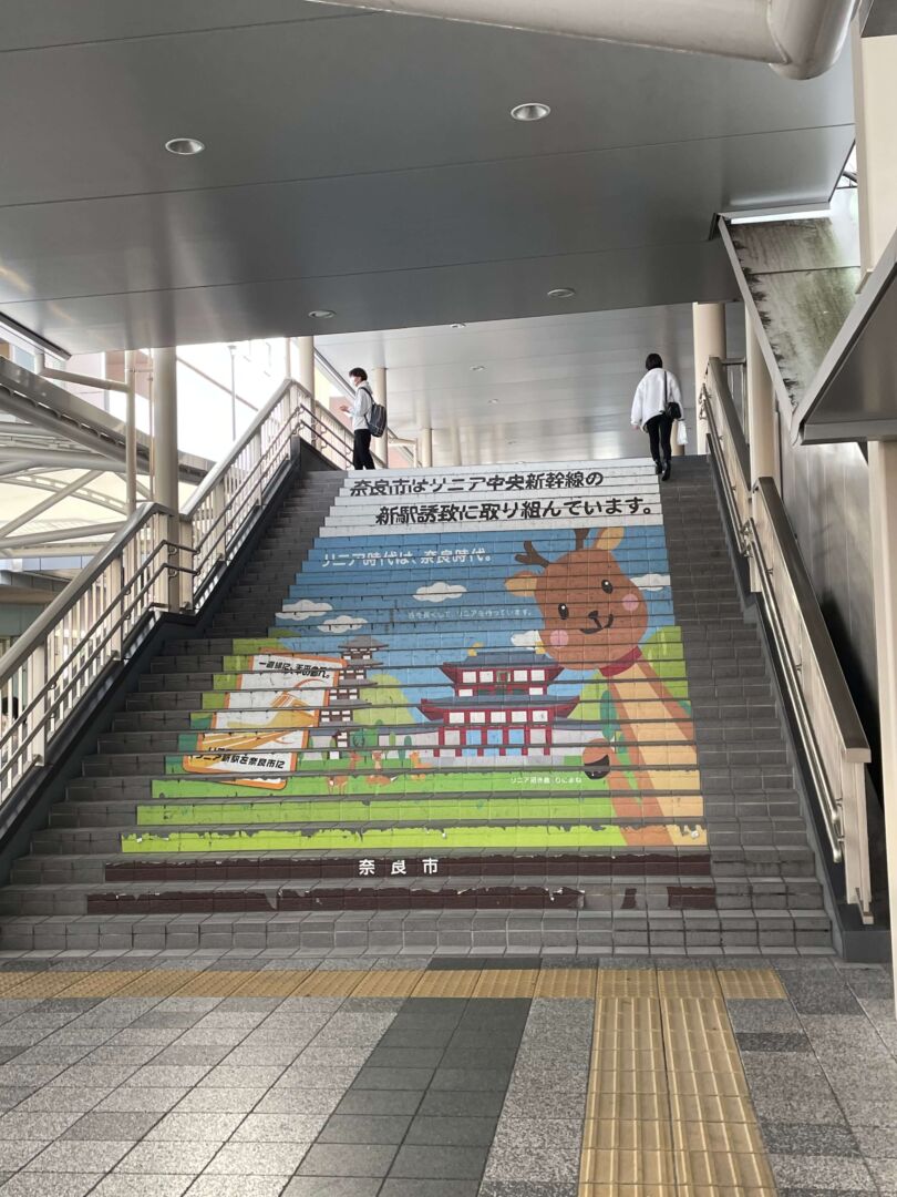 Escadas onde está adesivado palavras em japonês e o desenho de um cervo ao lado de um templo.