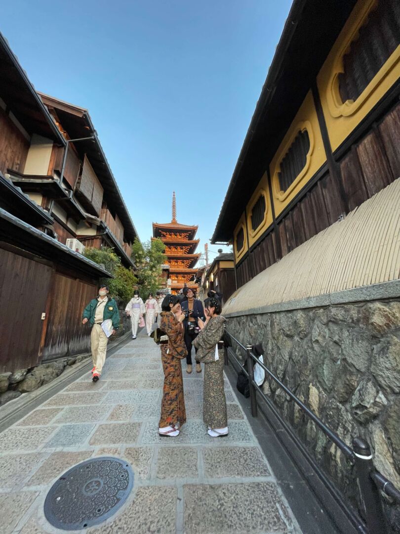 A Pagoda Yasaka ao fundo, nas laterais construções antigas e típicas e duas mulheres vestindo kimono estão na frente da foto.