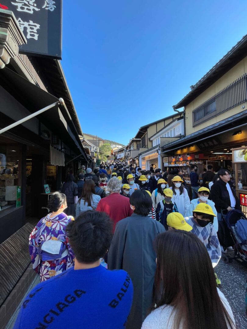 Na subida para chegar no templo, a rua está bem cheia de pessoas. Nas laterais, lojas abertas dentro de construções típicas japonesas.