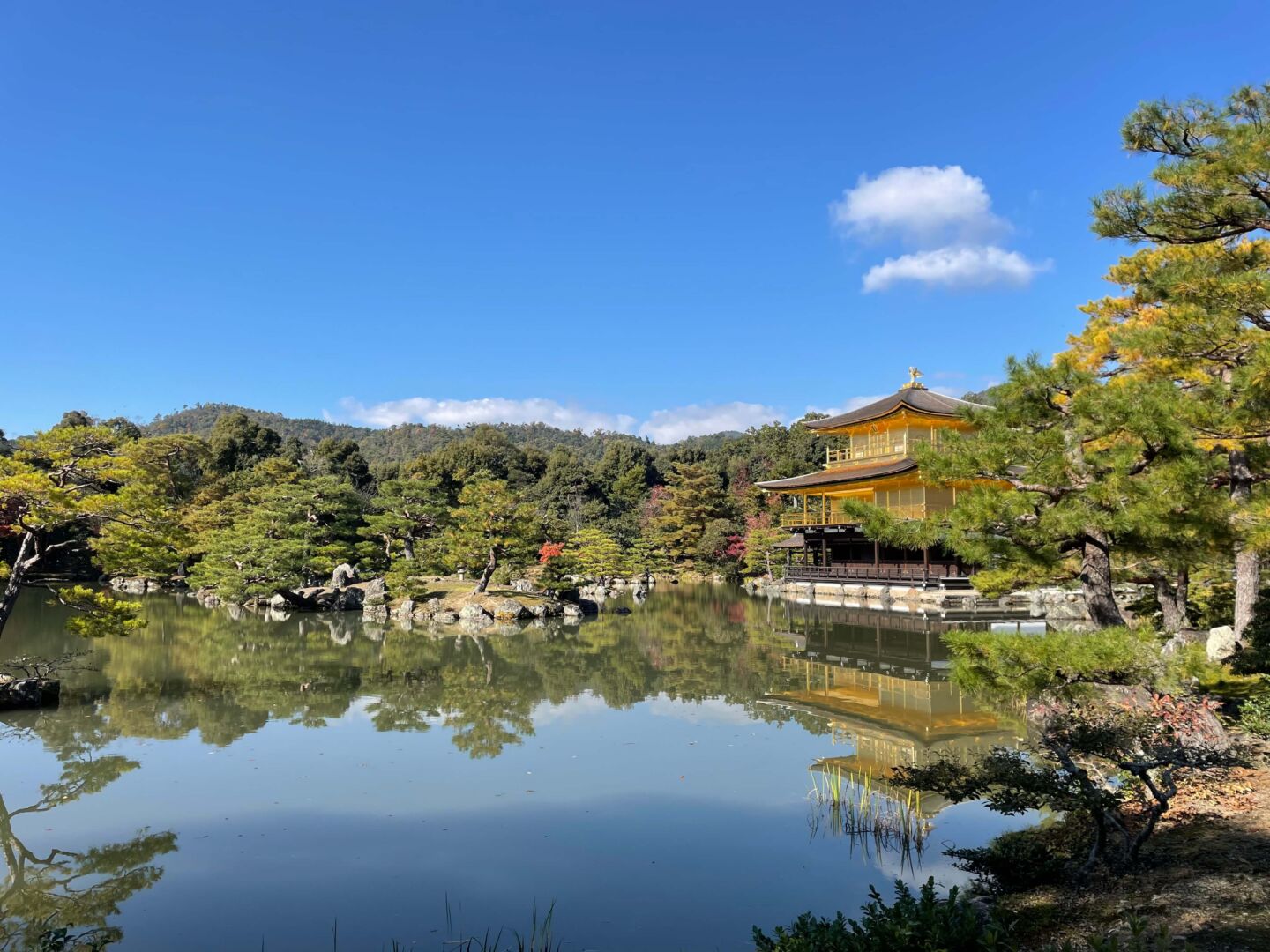 Um lago no centro reflete o céu azul, o templo no lado direito e as árvores verdes.