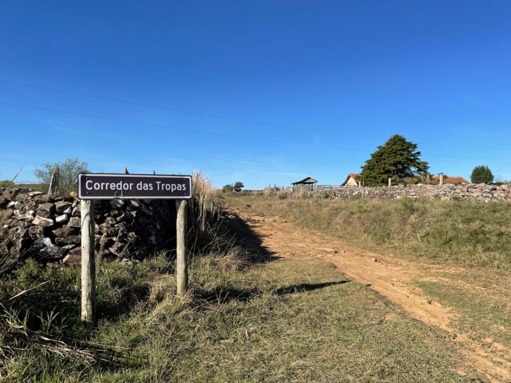 estrada de terra com muros de taipa e placa indicando corredor dos tropeiros